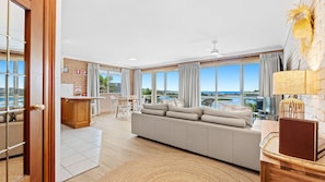 A spacious living area with a large sofa, a dining table, and a kitchen area. - Grand Pacific 1 Unit 1 - Ground Floor (NAROOMA)