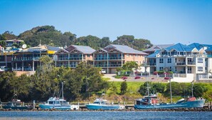 A coastal residential area with multiple two-story houses, a marina with boats, and a clear view of the water. - Grand Pacific 1 Unit 1 - Ground Floor (NAROOMA)