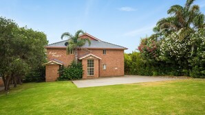 A two-story brick house with a front lawn and a driveway. - Grand Pacific 2 Unit 1 - Ground Floor (NAROOMA)