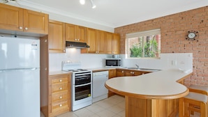 A kitchen with wooden cabinets, a built-in oven, a microwave, and a sink. - Grand Pacific 2 Unit 1 - Ground Floor (NAROOMA)