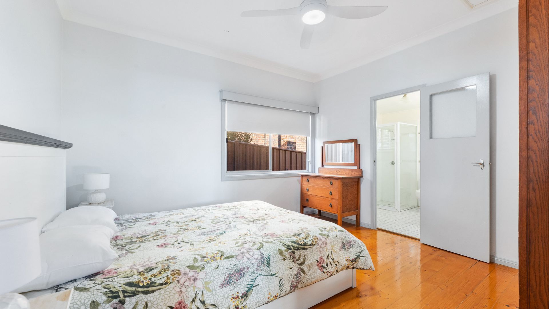 Une chambre à coucher comprenant un lit, une commode, une fenêtre et une porte donnant sur une salle de bain.
