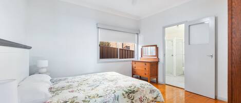 Une chambre à coucher comprenant un lit, une commode, une fenêtre et une porte donnant sur une salle de bain.
