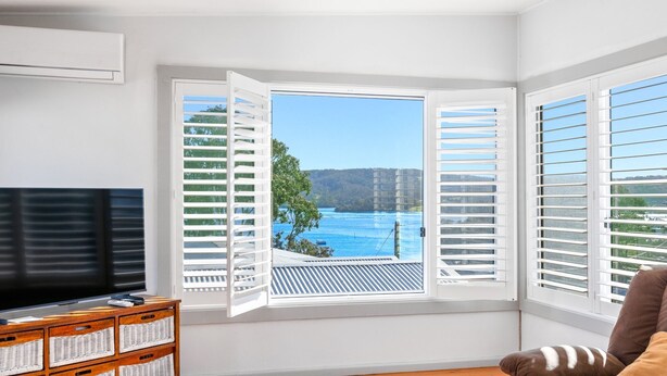 Ein Zimmer mit großem Fernseher, einem Holzkabinent und Blick auf ein blaues Gewässer durch offene Fenster.
