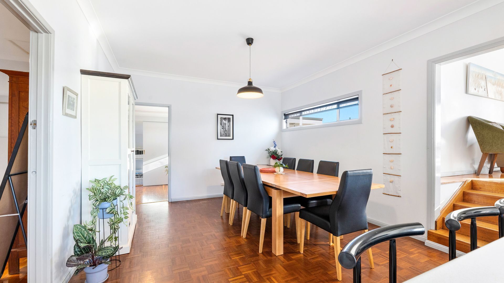 Uma  área de refeições com mesa de madeira, cadeiras pretas e uma luminária pendente.