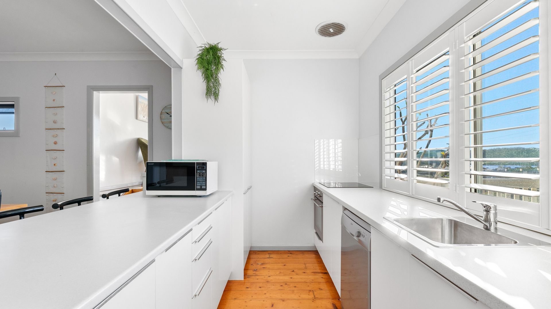 A modern kitchen with white cabinetry, a microwave, a sink, and a window with blinds.