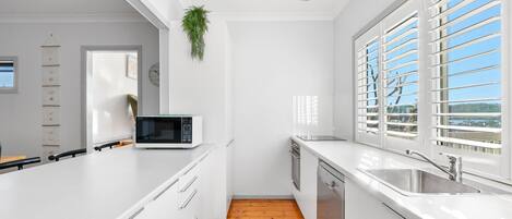 A modern kitchen with white cabinetry, a microwave, a sink, and a window with blinds.