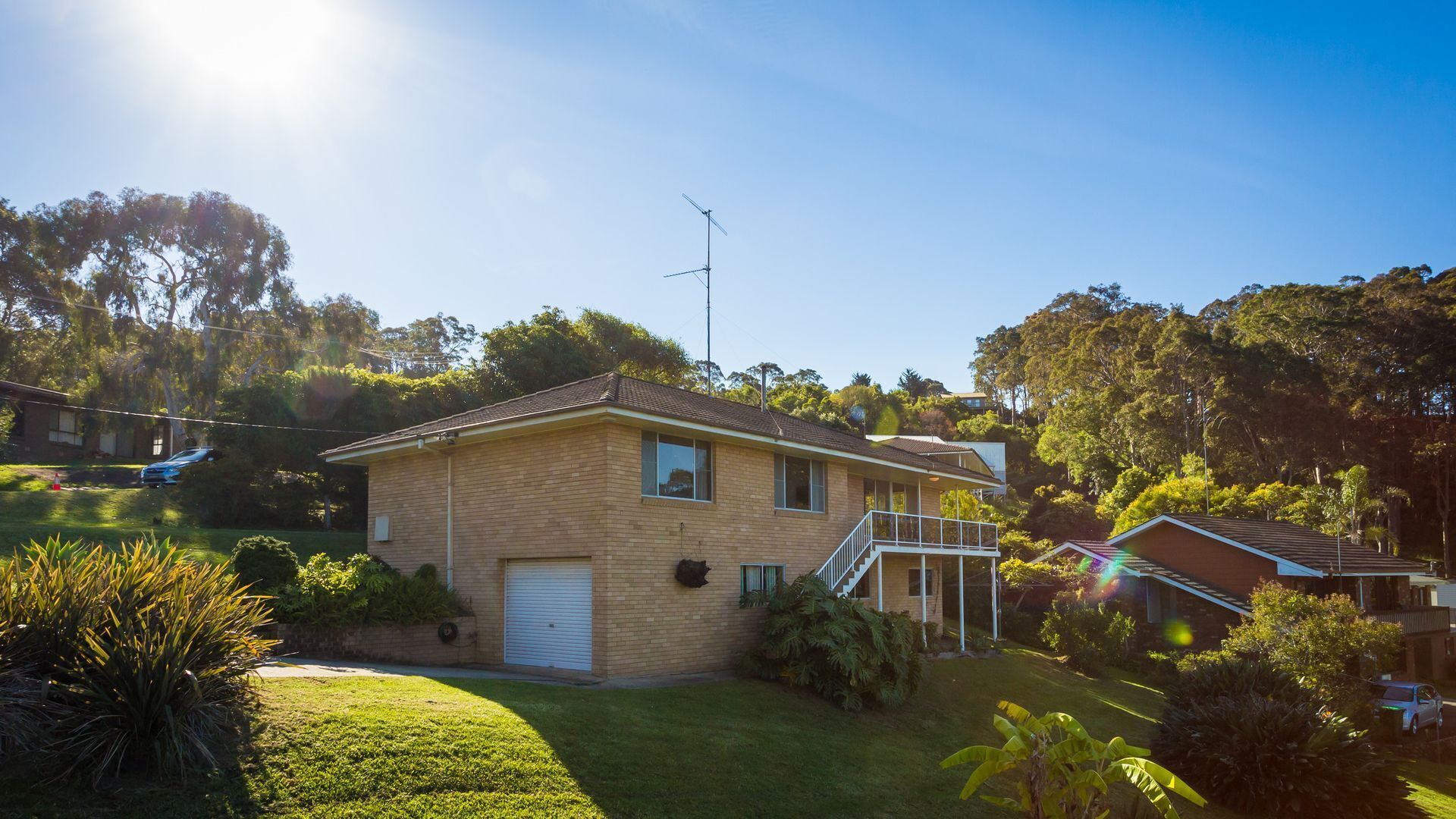 Une maison à deux étages avec un garage, entourée d’une végétation luxuriante et d’arbres.