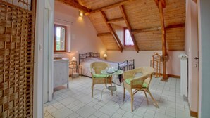 A cozy room with a sloped ceiling, a bed, wicker furniture, and a window. - Chambres d'hôtes Las Vignes (Beaucens)