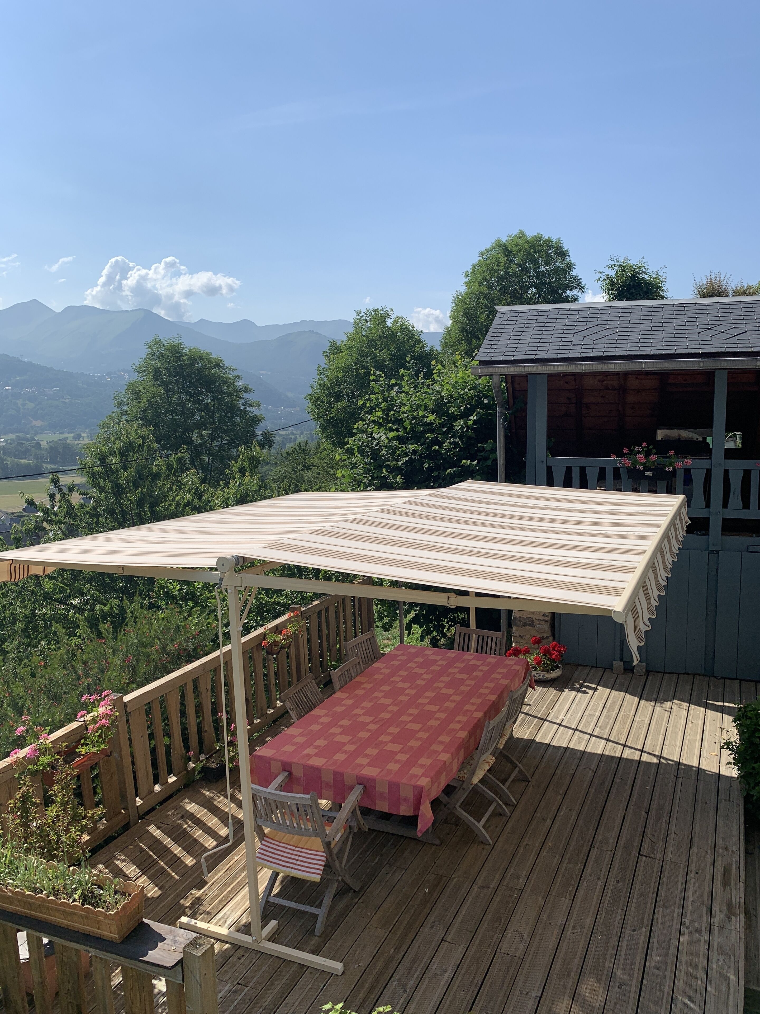 A wooden deck with a table and chairs, a pergola with a striped awning, and a view of mountains.