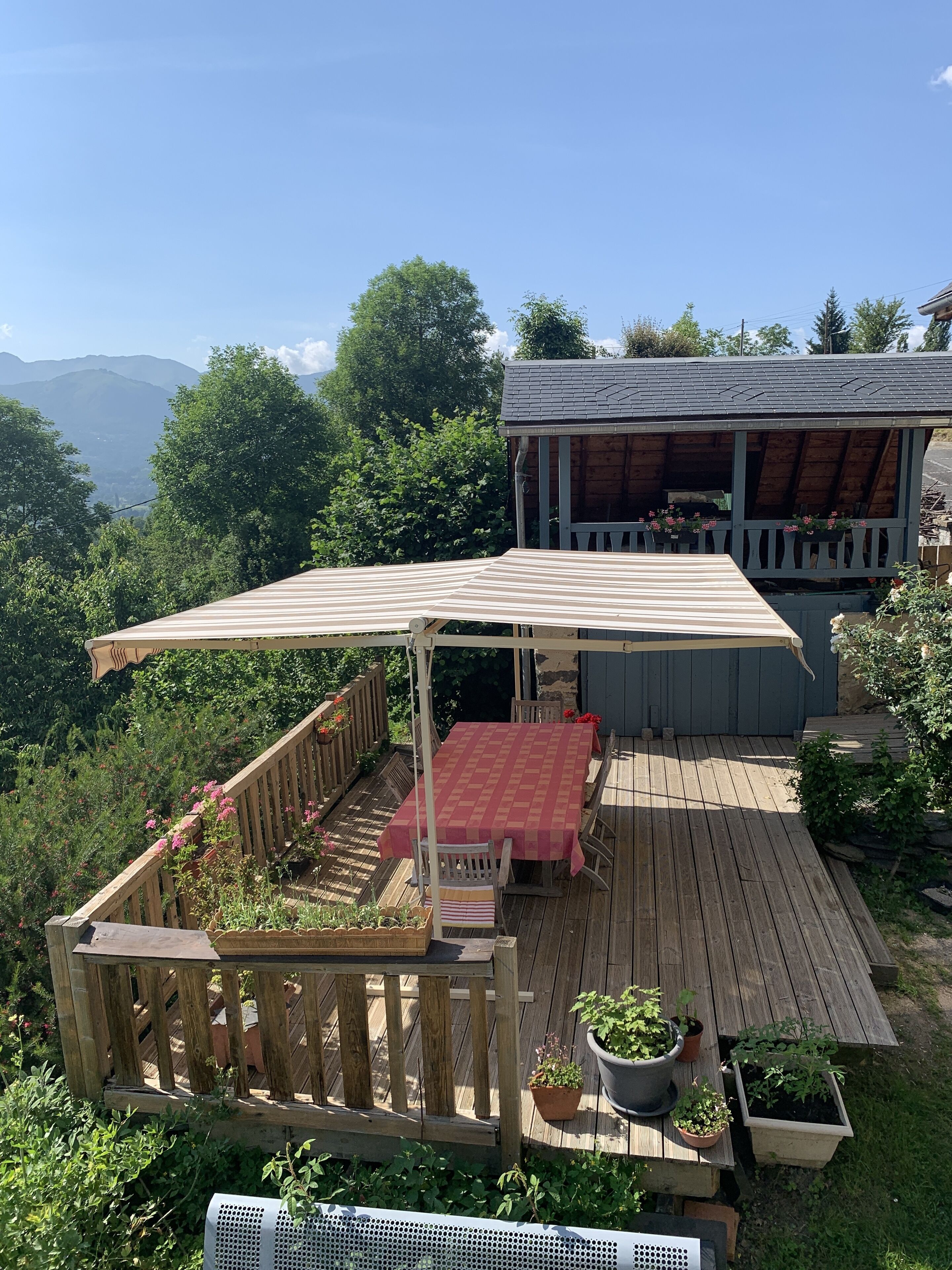 A wooden deck with a covered table and chairs, surrounded by potted plants and a wooden fence.
