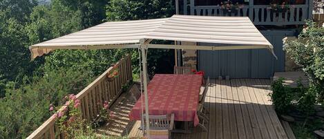A wooden deck with a covered table and chairs, surrounded by potted plants and a wooden fence.