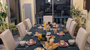 A dining area with a table set for a meal, surrounded by chairs, and a view of a kitchen through a glass door. - Chambres d'hôtes Las Vignes (Beaucens)