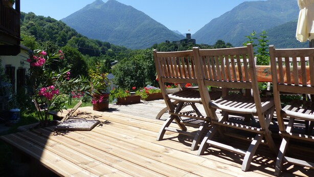 A wooden deck with a table and chairs overlooking a mountainous landscape. - Chambres d'hôtes Las Vignes (Beaucens)