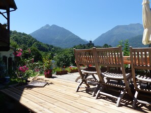 A wooden deck with a table and chairs overlooking a mountainous landscape. - Chambres d'hôtes Las Vignes (Beaucens)