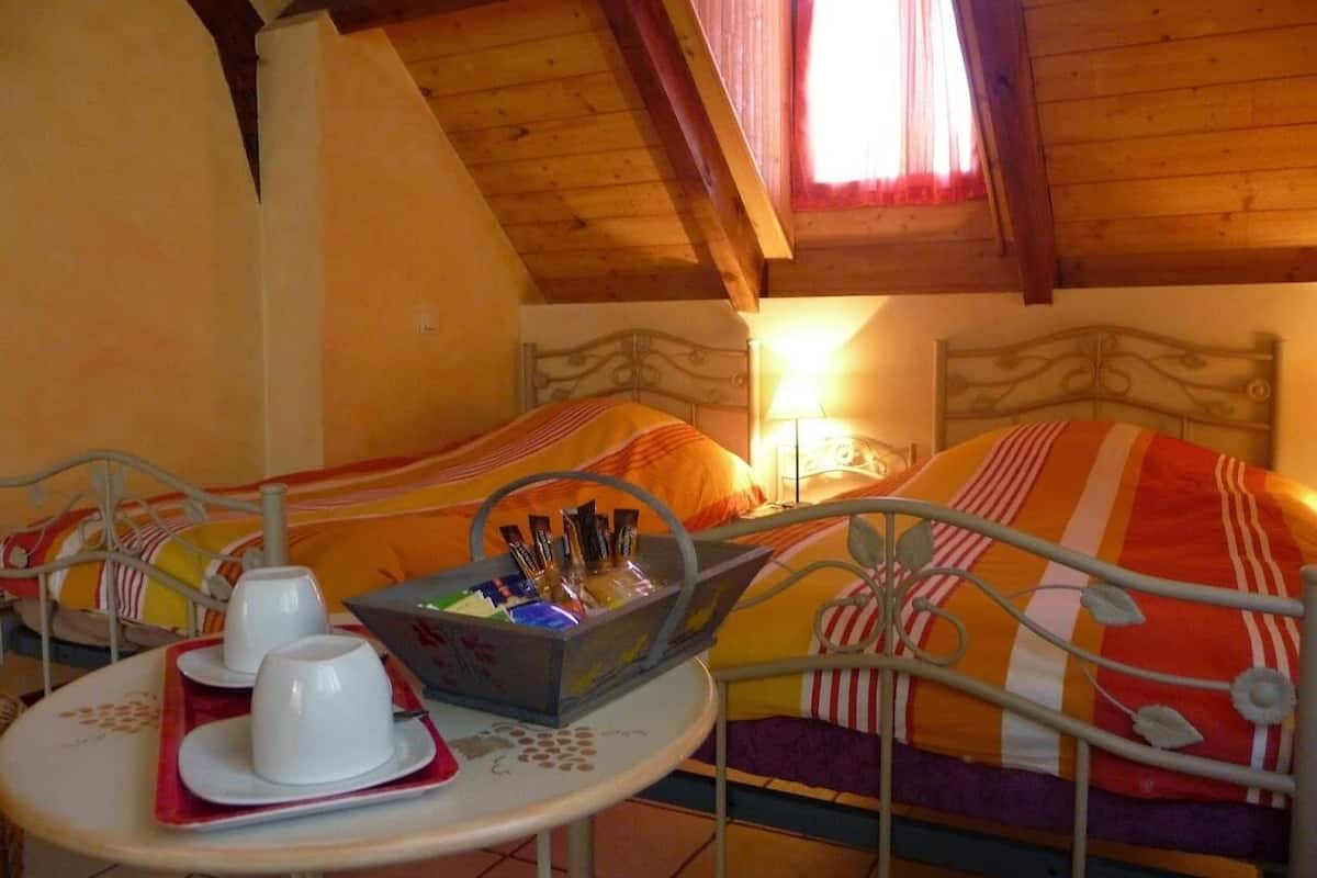 Una habitación acogedora con dos camas, una mesita con tazas y una cesta, y una ventana con cortinas.