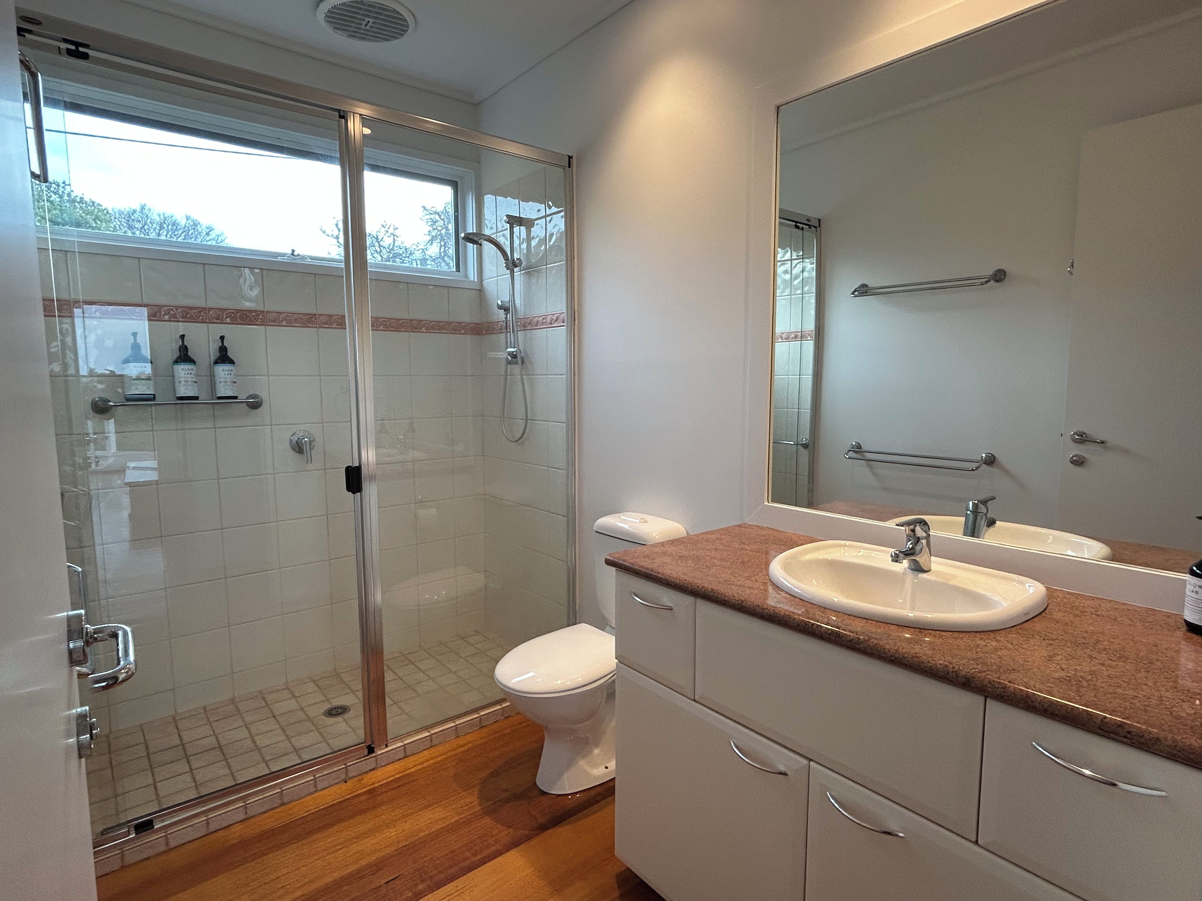 A modern bathroom with a glass-enclosed shower, a white toilet, and a vanity with a sink and mirror.