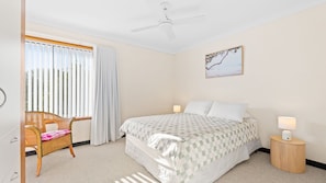 A hotel room with a bed, a chair, a nightstand, a ceiling fan, and a window with curtains.