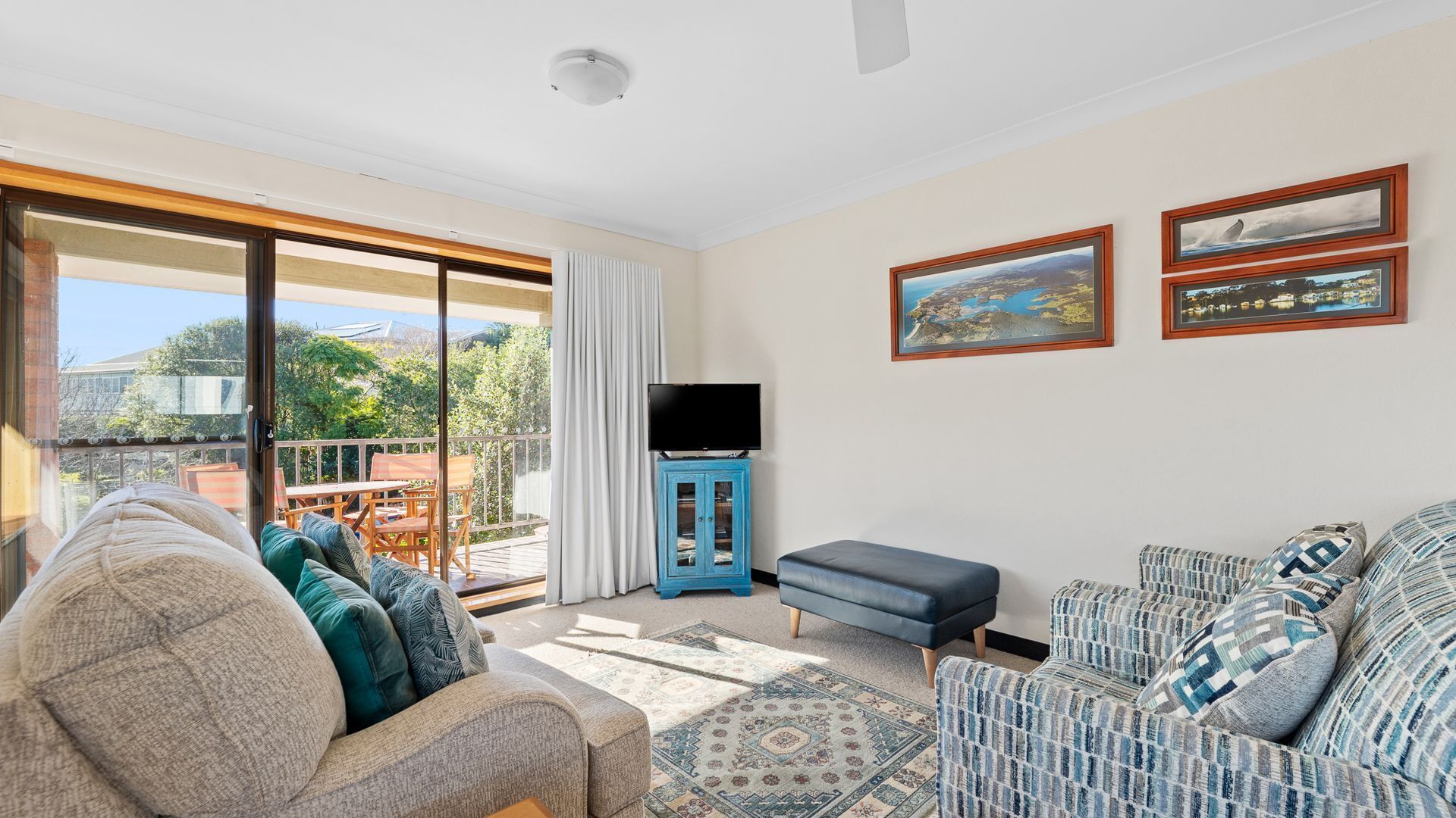 A living room with a sofa, a blue cabinet with a television, and two framed pictures on the wall.