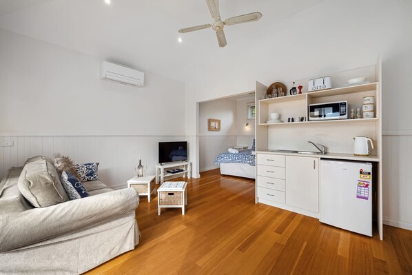 A compact living space with a sofa, TV, kitchenette, and a ceiling fan.