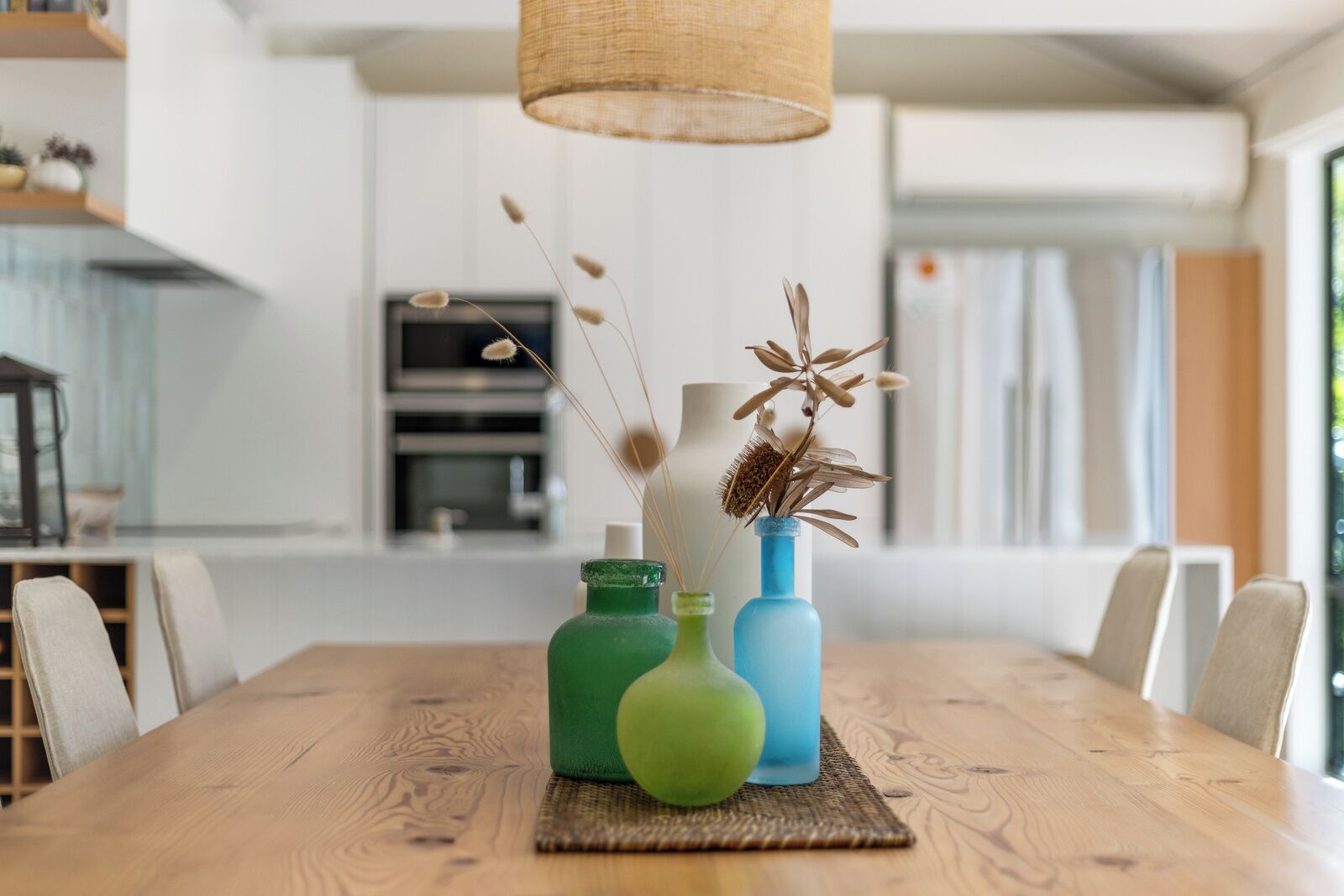 A wooden dining table with three glass vases containing dried plants.
