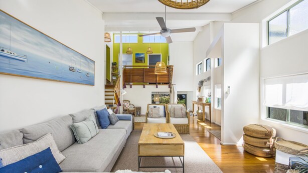 Ein geräumiges Wohnzimmer mit grauem Sofa, einem Holztisch und Blick auf einen grünen Dachbodenbereich.