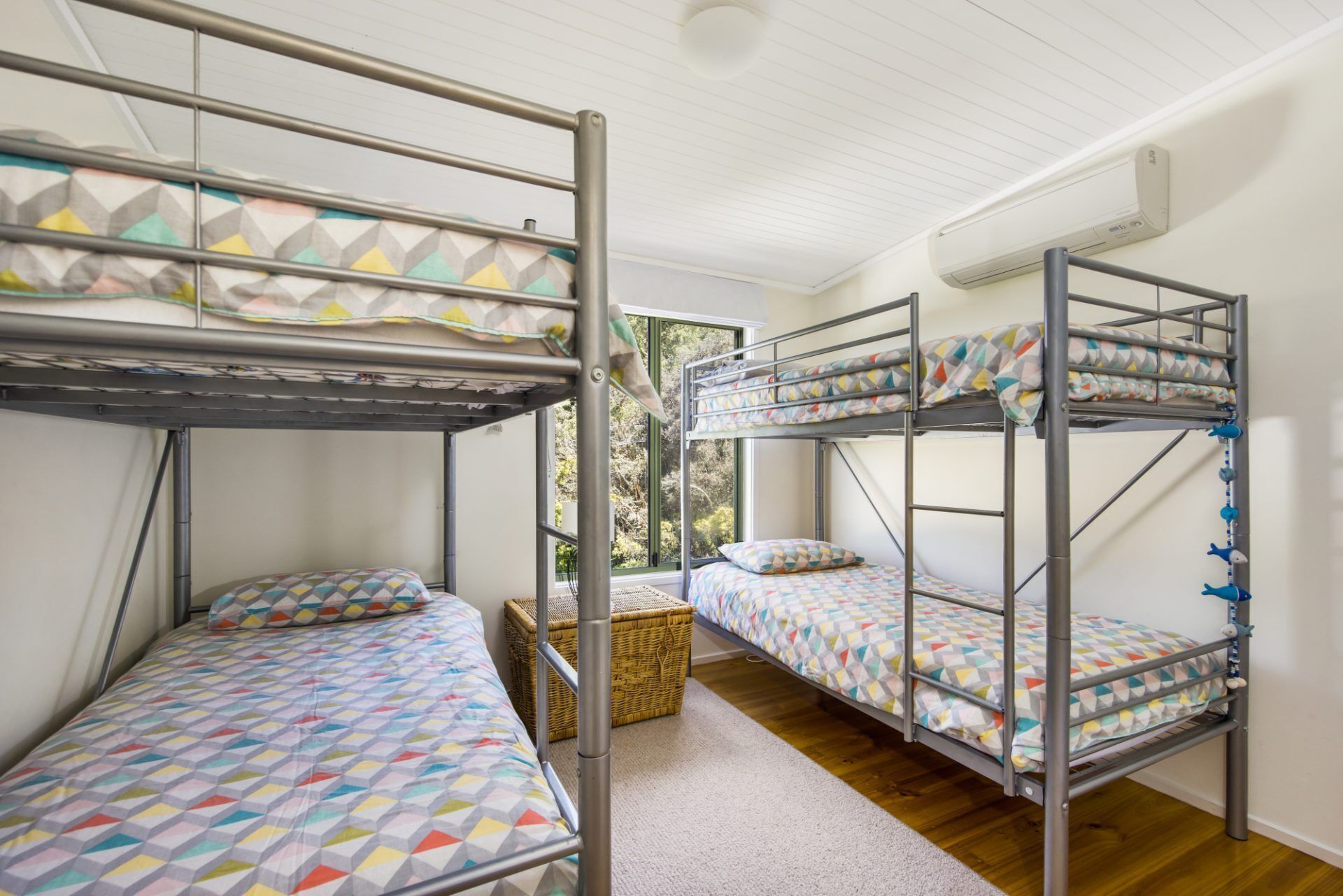 A dormitory room with bunk beds, a wicker basket, and a window with a view of greenery.