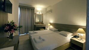 A hotel room with two beds, a TV, a desk with a vase of flowers, and a bathroom visible through a door. - Apollon Hotel - Adults Only (Agios Nikolaos)