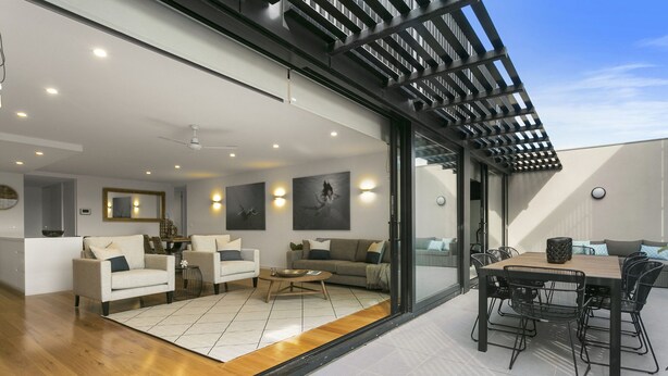 Un espace de vie moderne doté d’un plancher en bois, d’un ensemble de canapés, d’un coin repas avec une table et des chaises, et d’un ventilateur de plafond.