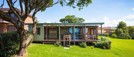 A modern log cabin with a deck, surrounded by a well-maintained lawn and a large tree.