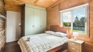 A bedroom with a bed, a wardrobe, a nightstand, and a window with a view of greenery.