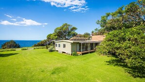A single-story house with a covered porch, a lawn, and a view of the ocean.