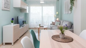 A modern living room with a sofa, a dining table with a plant, a TV on a cabinet, and a window with sheer curtains. - Apartment with sea view, parking, wifi (Marbella)