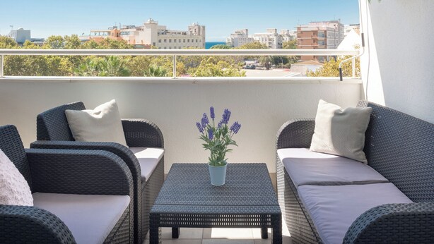 A balcony with wicker furniture, a table with a potted lavender plant, and a cityscape view. - Apartment with sea view, parking, wifi (Marbella)