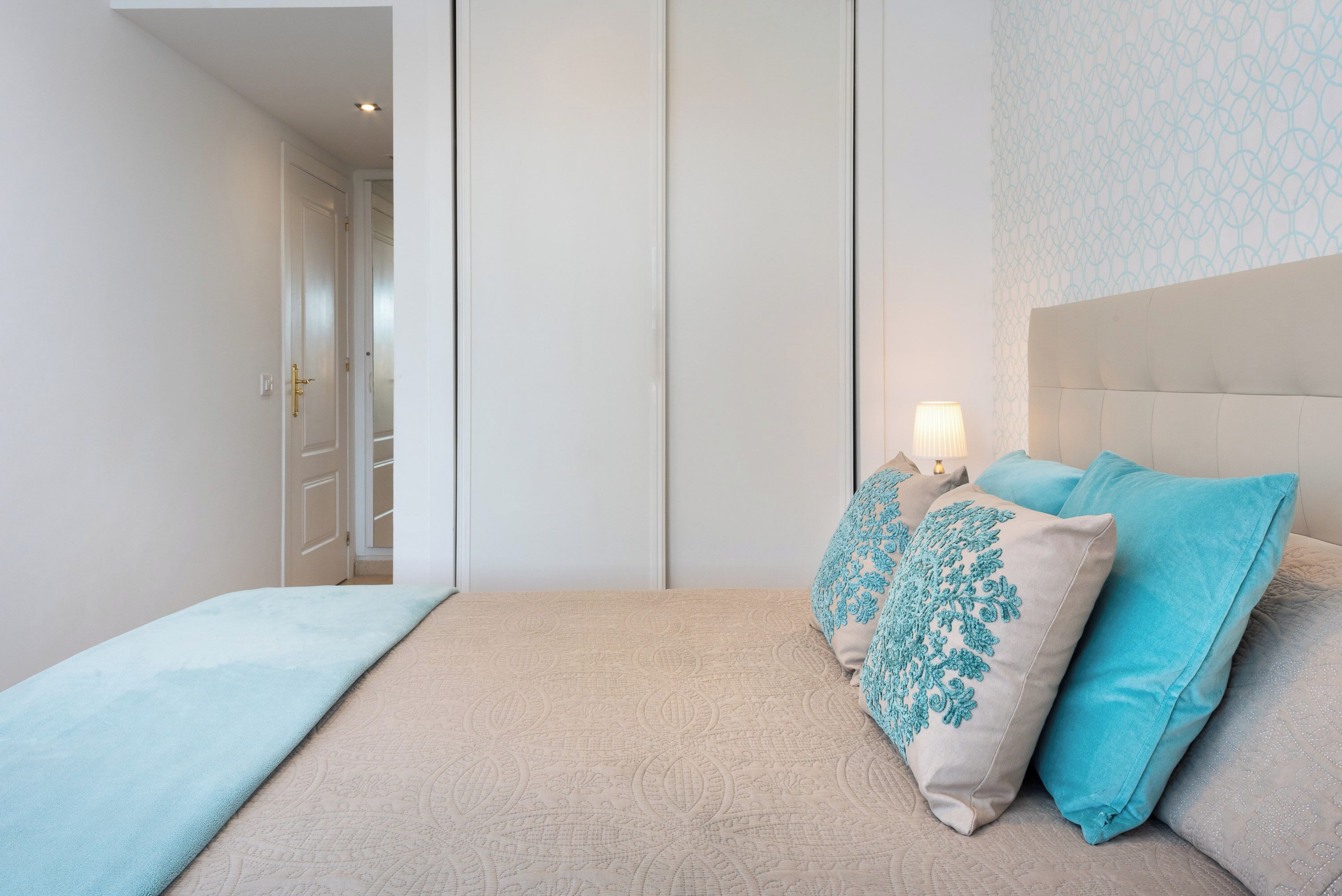 A bedroom with a bed, a nightstand, a lamp, and a patterned wall.