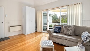 A modern living room with a grey sofa, a small white side table, and a glass coffee table. - ST PAULS PINK BAYSIDE SELF CONTAINED COTTAGE IN SORRENTO (Sorrento)