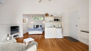 A compact, well-lit room with a bed, a TV, a kitchenette, and a ceiling fan. - ST PAULS PINK BAYSIDE SELF CONTAINED COTTAGE IN SORRENTO (Sorrento)
