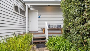 A house entrance with a white door, a small porch with a bench, and a hedge. - ST PAULS PINK BAYSIDE SELF CONTAINED COTTAGE IN SORRENTO (Sorrento)