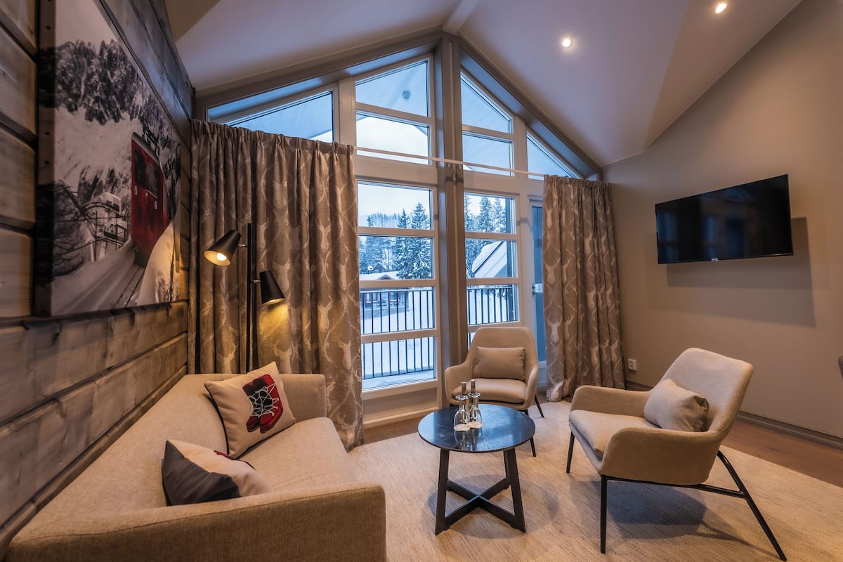 A modern living room with a large window, a flat-screen TV, and a cozy seating area.