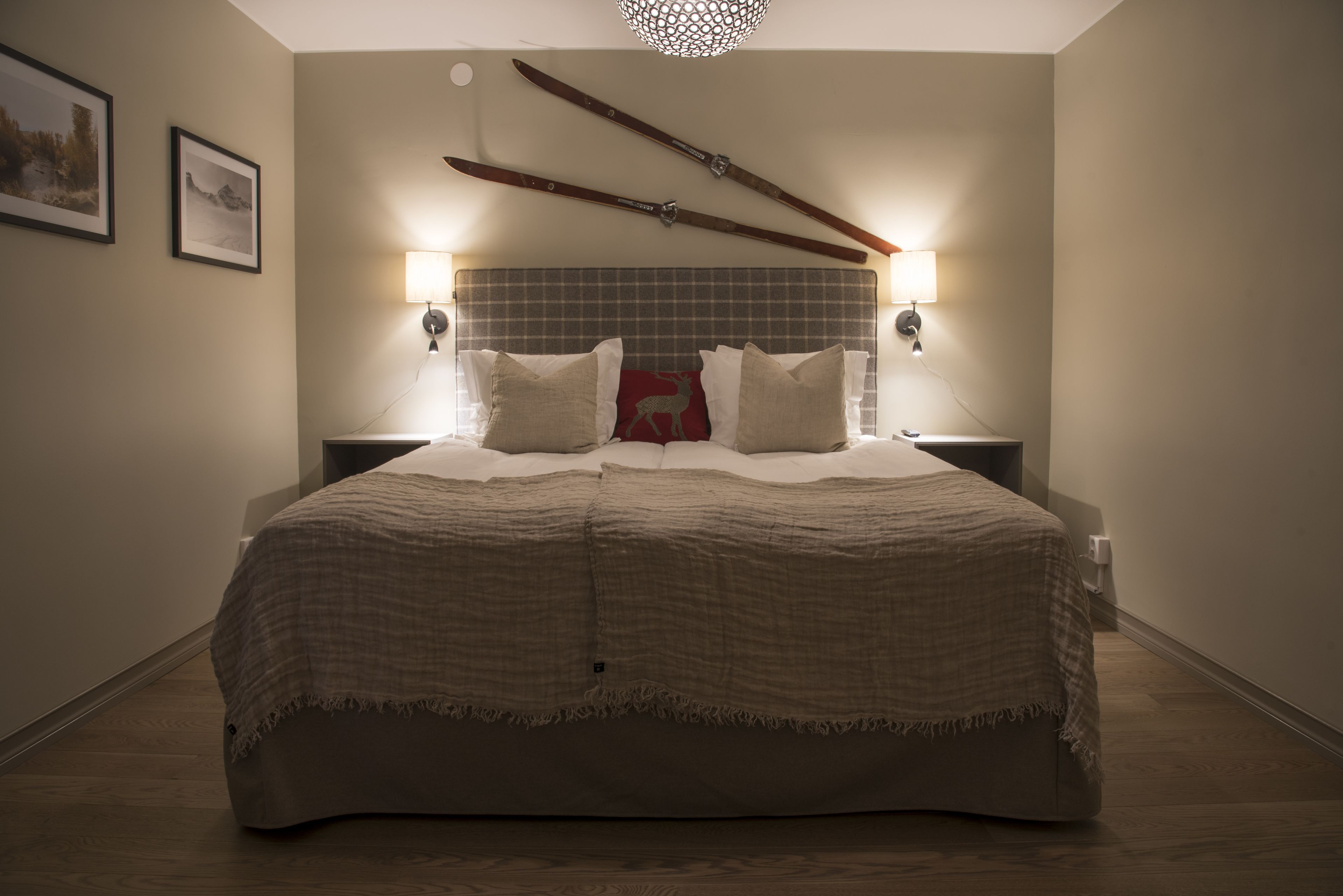 A neatly made bed with a checkered blanket, two pillows, and a red decorative pillow. There are two wall-mounted lights on either side of the bed.