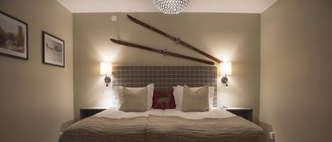 A neatly made bed with a checkered blanket, two pillows, and a red decorative pillow. There are two wall-mounted lights on either side of the bed.