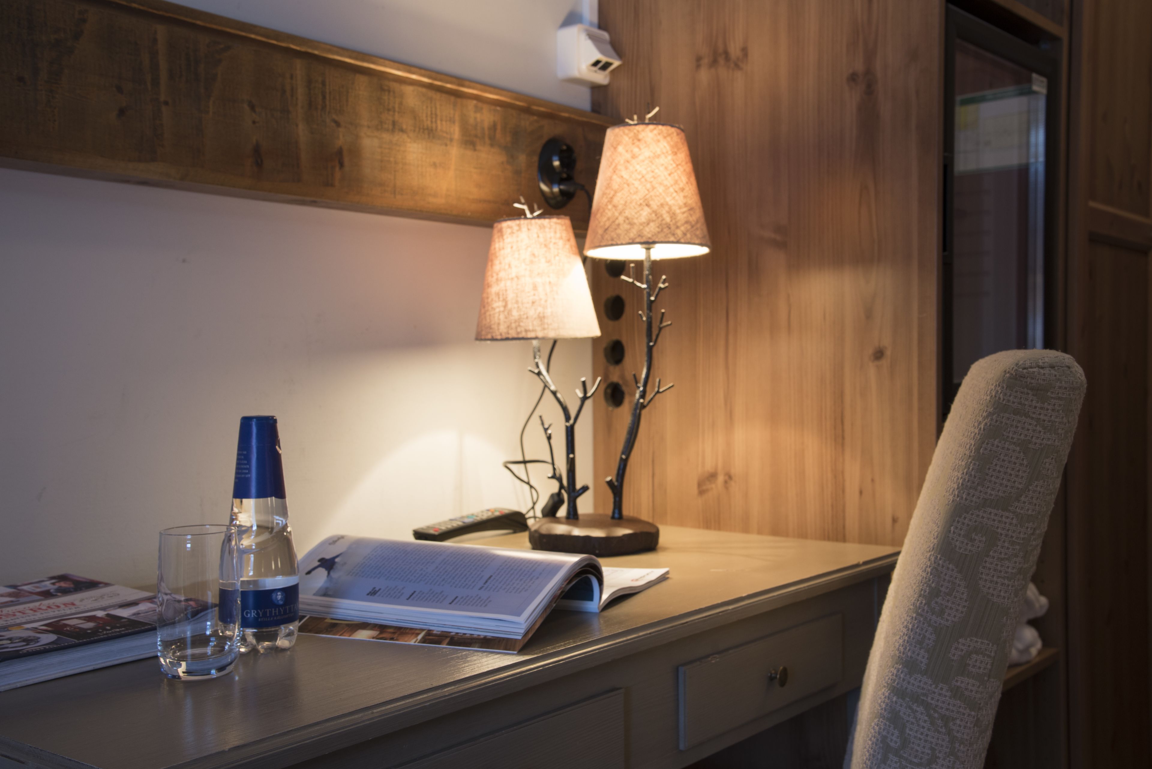 Ein Holztisch mit einer Lampe, einer Flasche, einem Glas und einem offenen Buch.