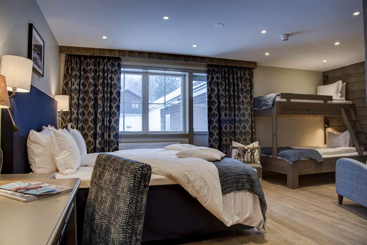 A hotel room with a large bed, a desk, and a bunk bed.