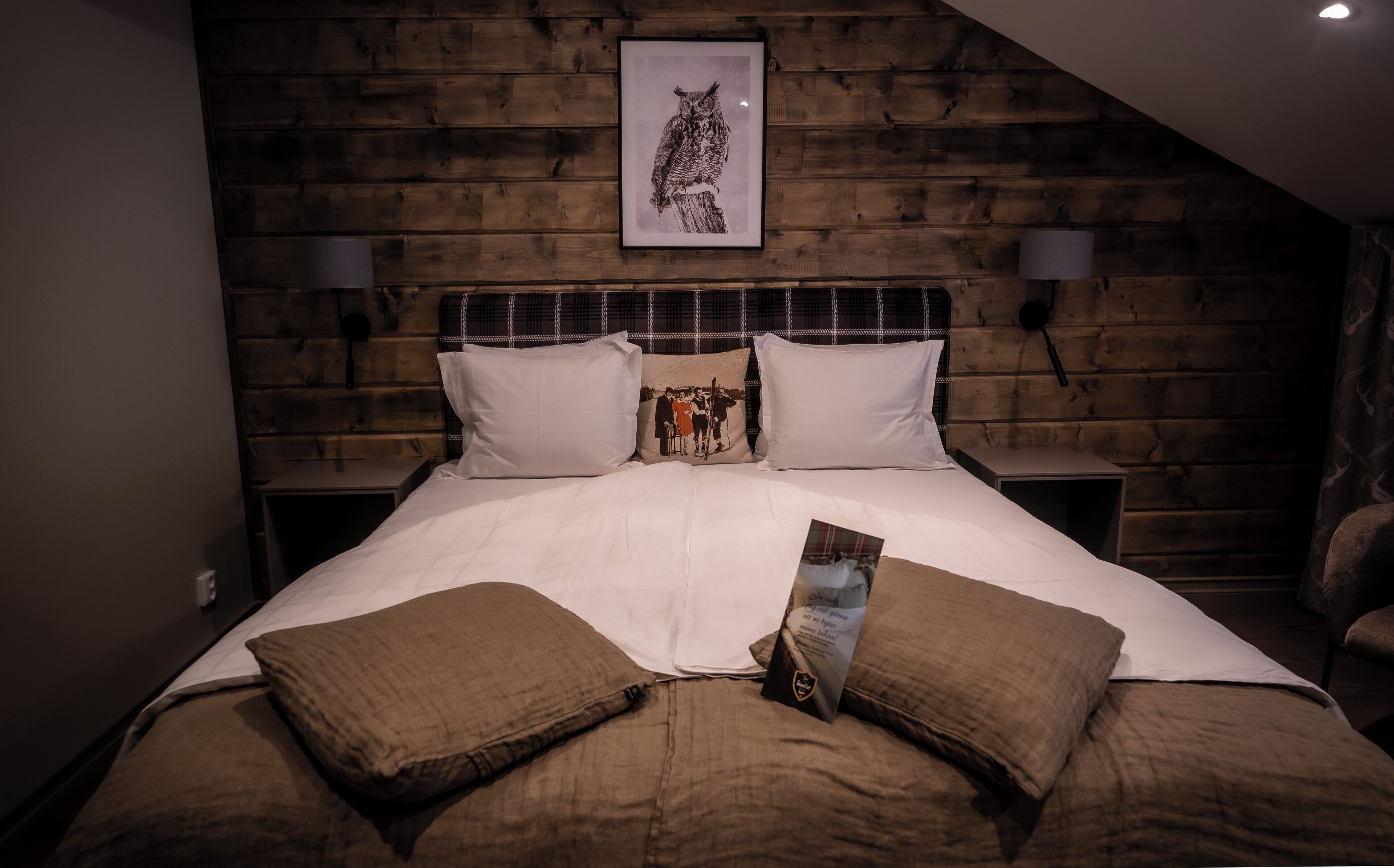 A bedroom with a wooden headboard, white bedding, and a framed picture of an owl.