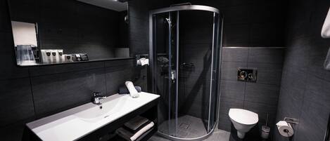A modern bathroom with a curved glass shower enclosure, a white sink, and a toilet.