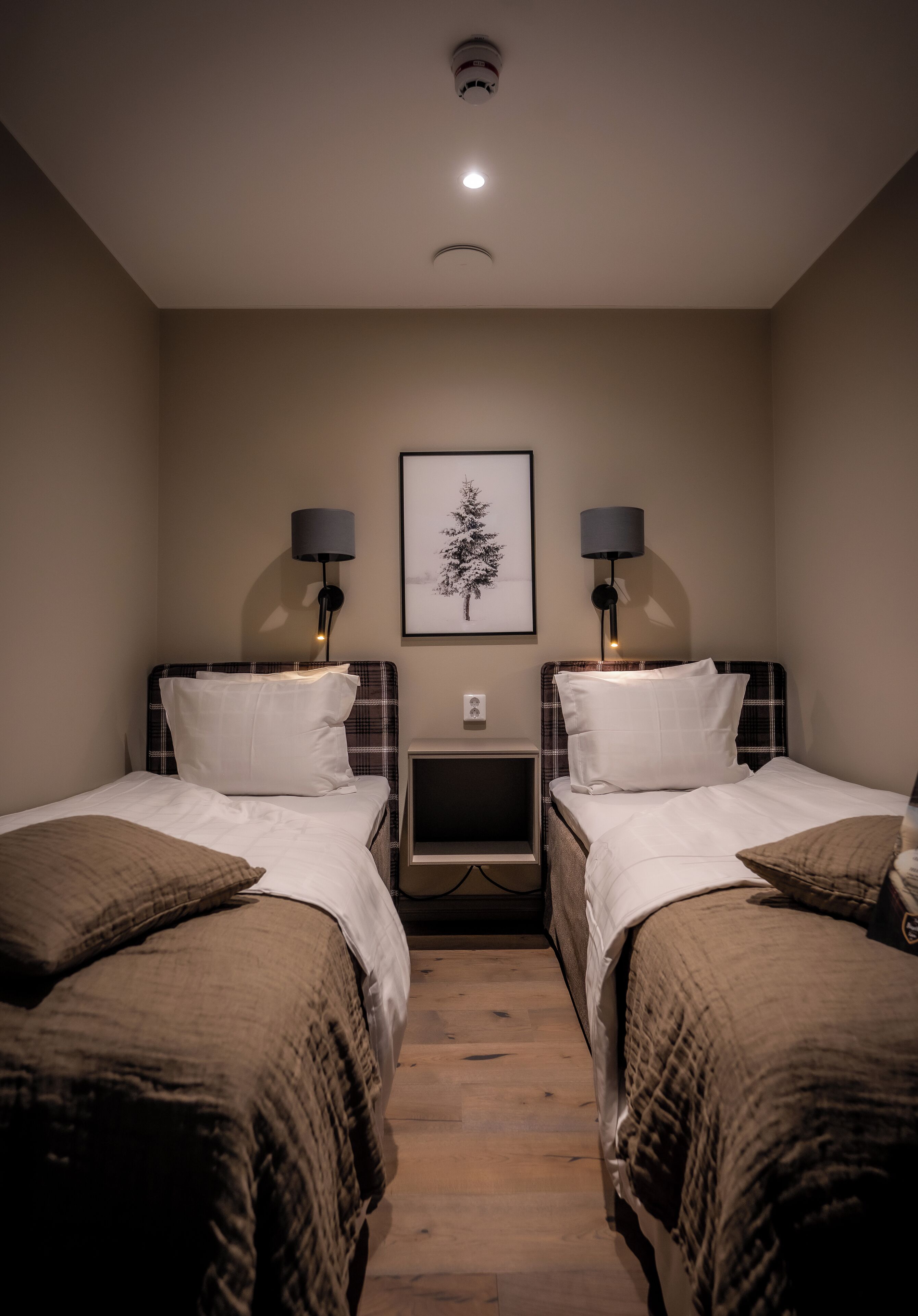 A hotel room with two beds, each with a headboard, bedside tables, lamps, and a framed picture on the wall.