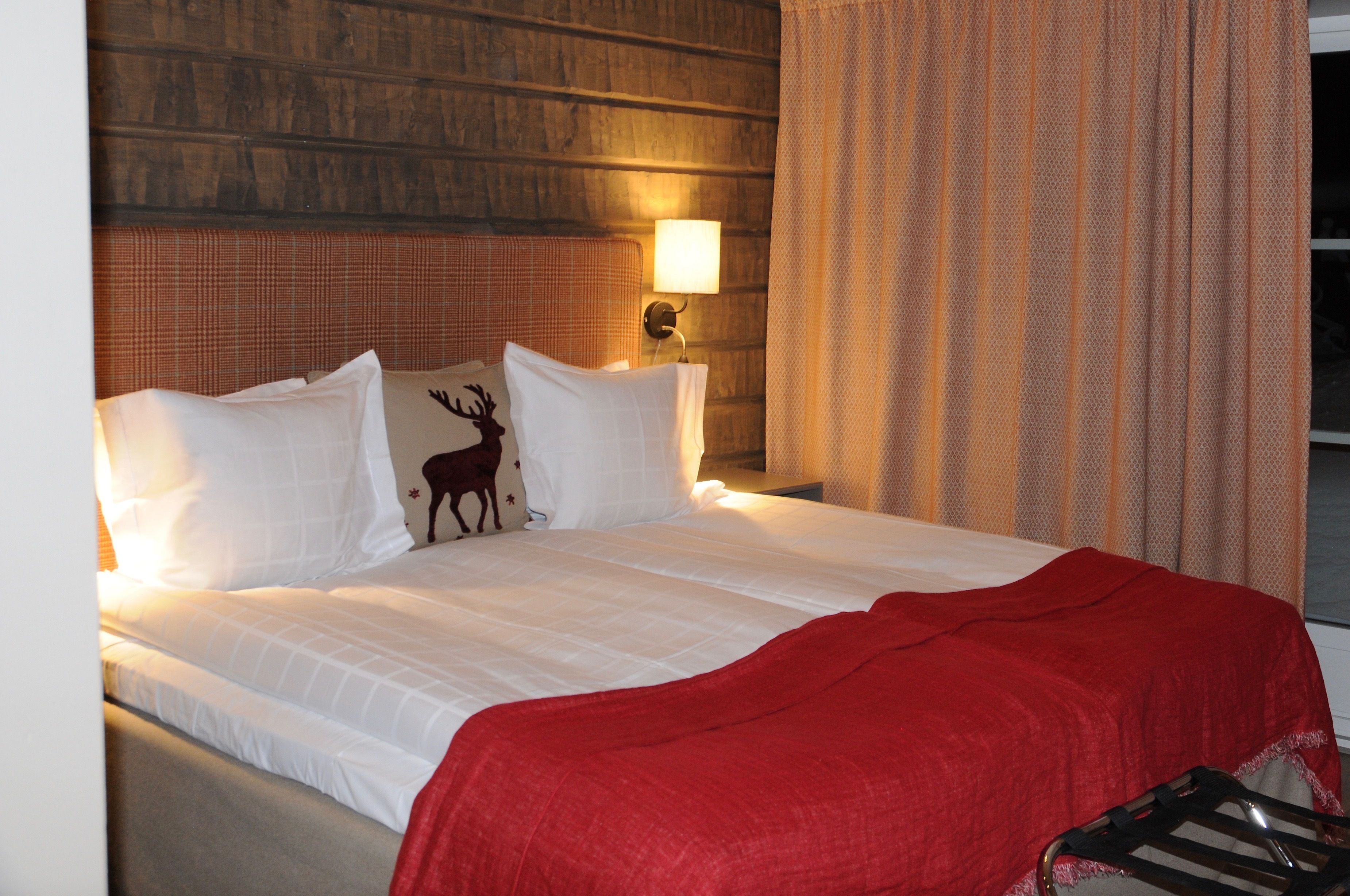 Ein Hotelzimmer mit Bett, einer roten Decke, einer Lampe und einem Vorhang.