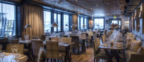 A restaurant with wooden floors, large windows, and a long dining table set for a meal.