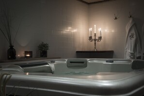 Um quarto de spa com uma banheira de hidromassagem, um castiçal fixado na parede com velas e um porta-toalhas.