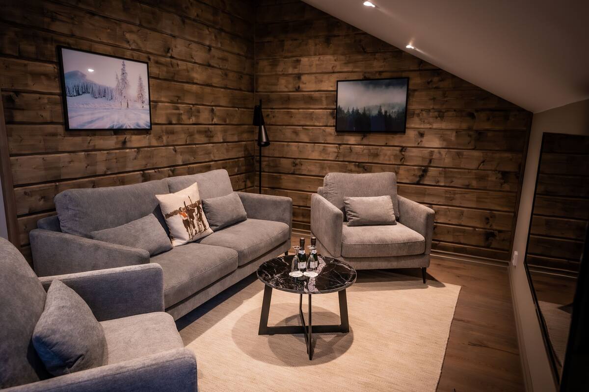 A cozy living room with a grey sofa, a grey armchair, and a black coffee table with bottles.