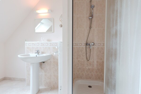 A bathroom with a pedestal sink, a shower with a handheld showerhead, and a mirror above the sink. - Villa Tracy (Tracy-sur-Mer)